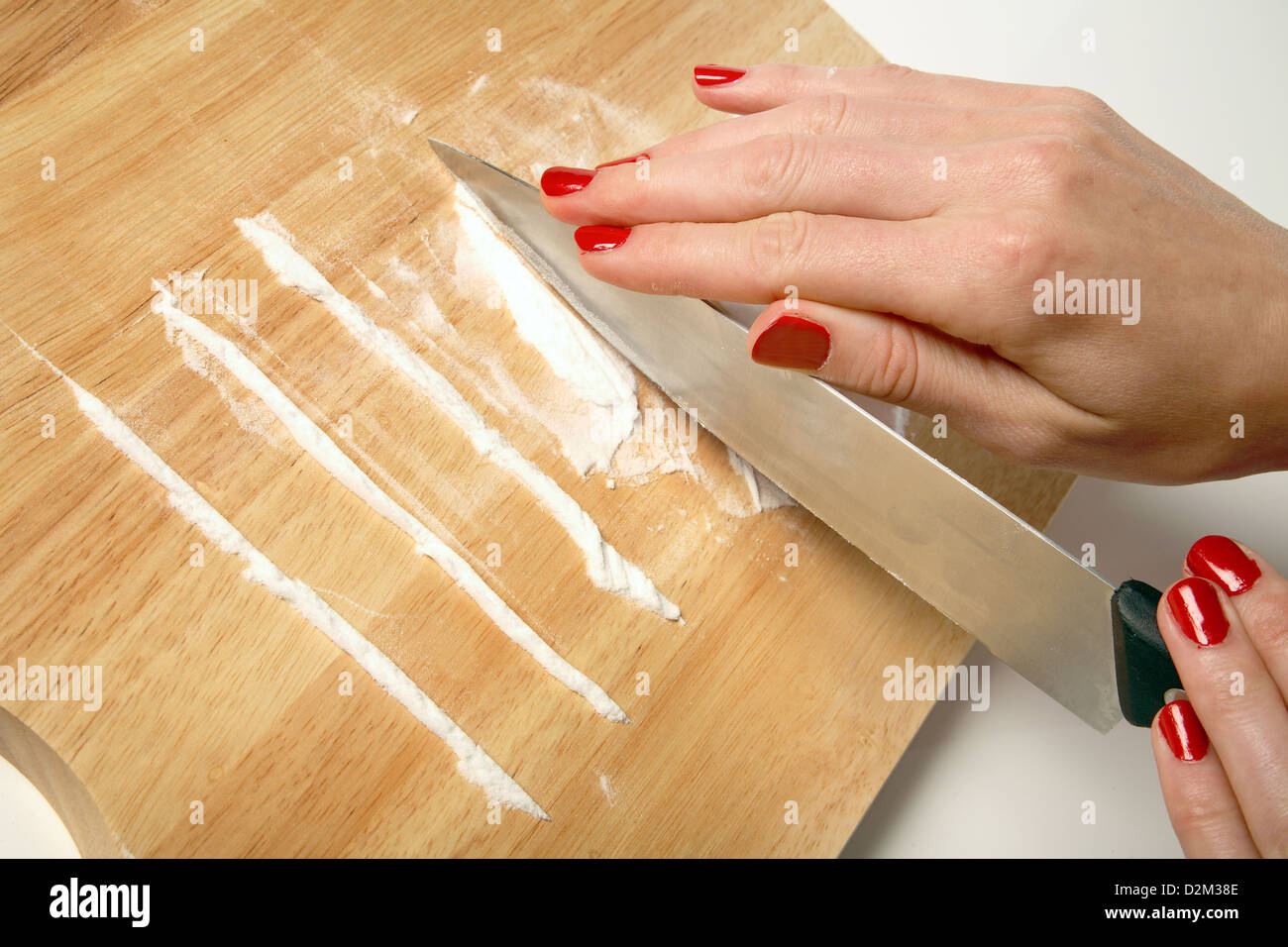 Una donna con il rosso smalto per unghie preparare una linea di cocaina su un tagliere di legno. Foto Stock