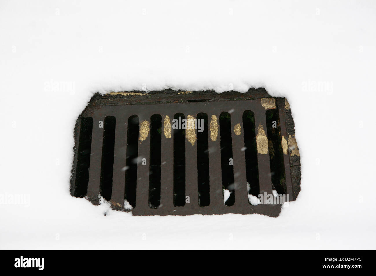 Neve posa su una strada con una ghisa coperchio di scarico che non ha nessuna neve su di esso. Foto Stock