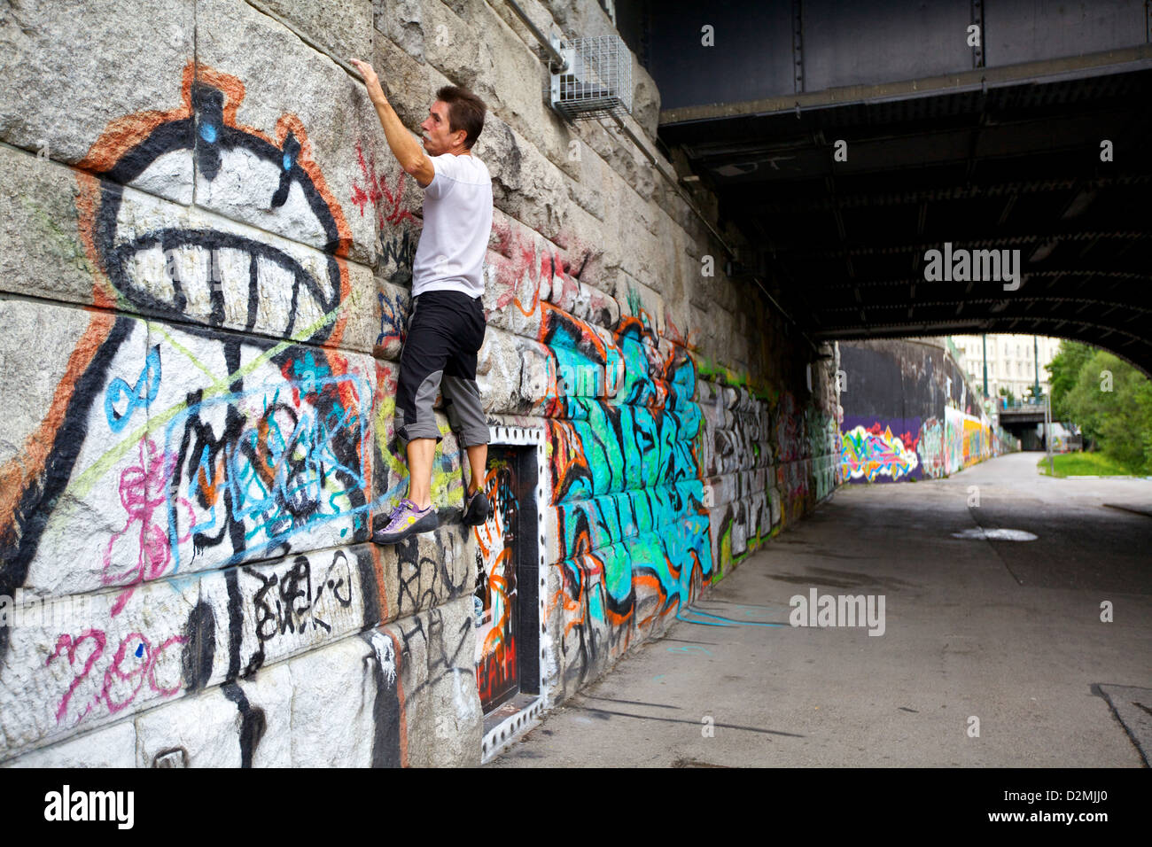 Un atleta di roccia scala un muro coperto di graffiti lungo il Danubio a Vienna, Austria, mescolando arte urbana e avventura all'aria aperta Foto Stock