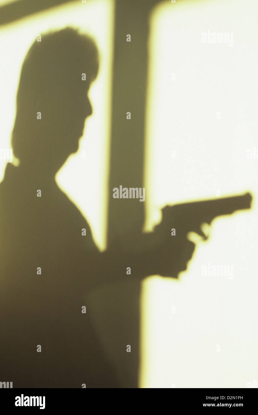 Ombre sul muro bianco del telaio della finestra con la donna pistola di puntamento Foto Stock