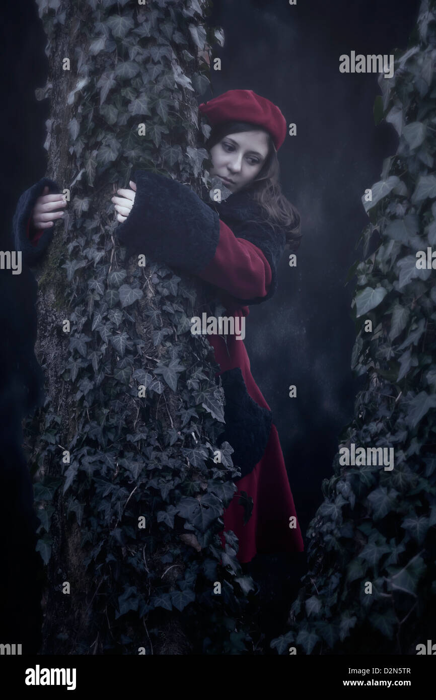 Una donna in un rivestimento di colore rosso è abbracciando un vecchio albero con edera Foto Stock
