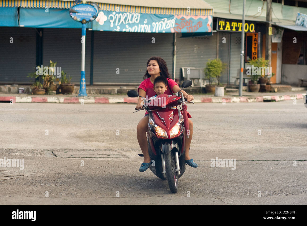 Una donna che cavalca un ciclomotore con un bambino in Thong Sala , Koh Phangan , della Thailandia Foto Stock