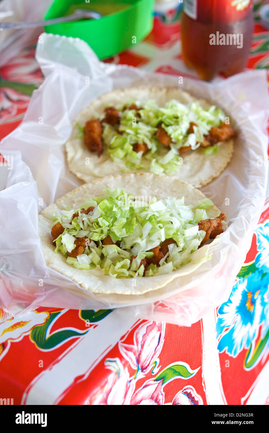 Tacos di pesce appena sfornato con lattuga grattugiata, serviti su una tovaglia colorata a Mazatlán, Sinaloa, Messico Foto Stock