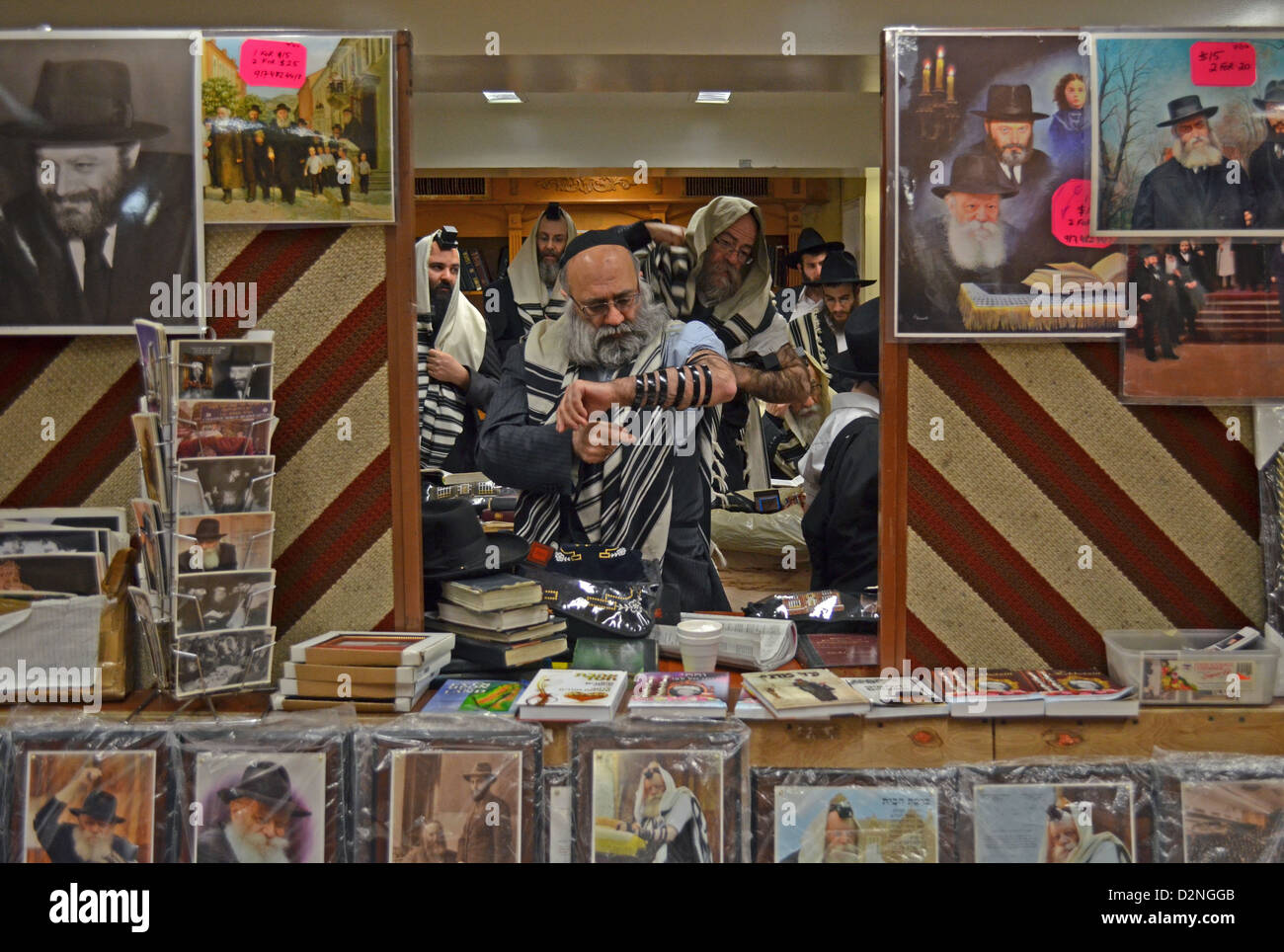 Incorniciato da foto per la vendita del Rebbe, un uomo mettendo in teffilin al mattino servizi a Lubavitch sede a Brooklyn Foto Stock