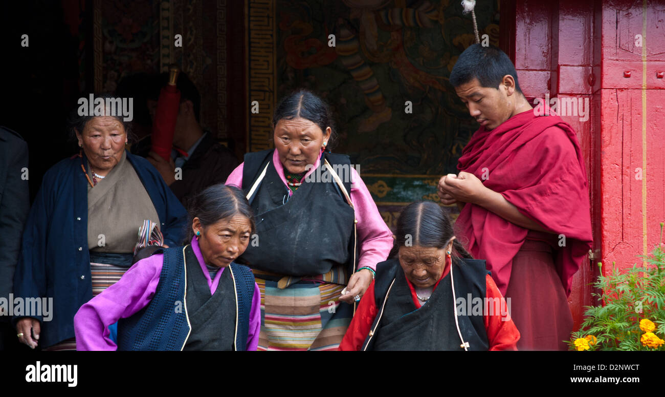 Donne pellegrini lasciando Sutra Hall con Monaco di guardia ingresso, Monastero Tashilhunpo, Shigatse, nel Tibet Foto Stock