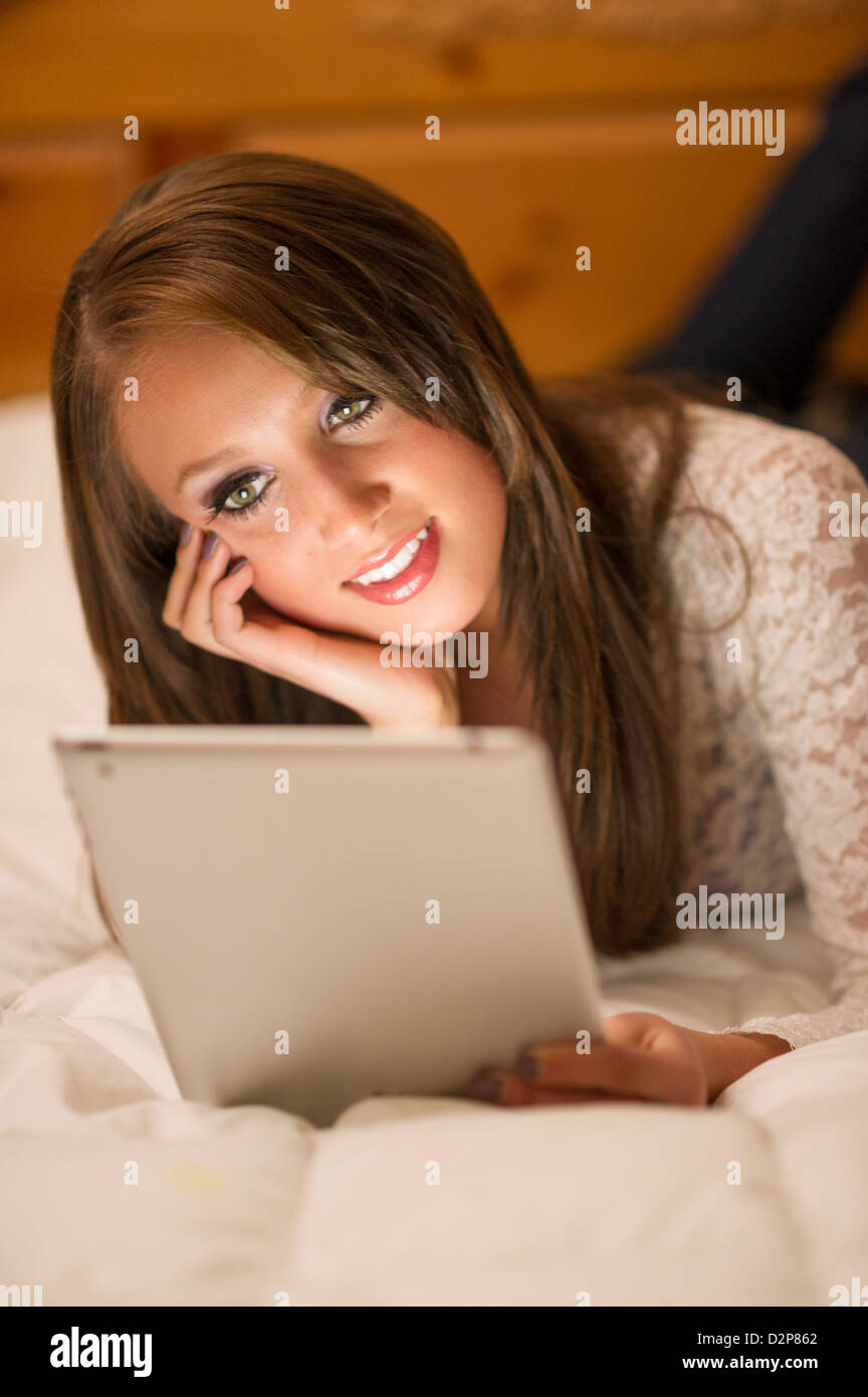 Bella ragazza adolescente giacente su un letto lavorando su un computer tablet. Foto Stock