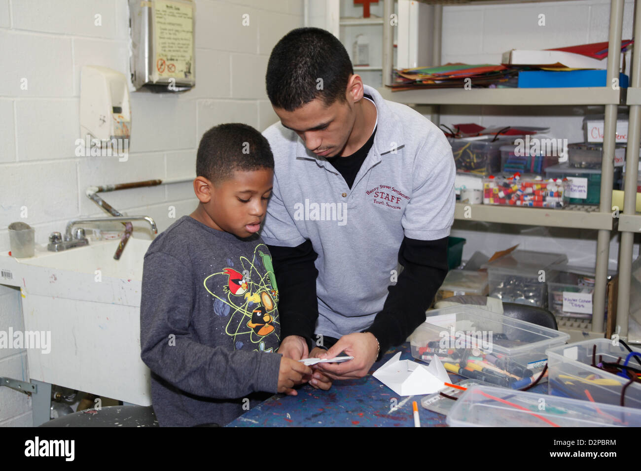 Alta scuola ragazzo di età lavora con i bambini più piccoli in un percorso educativo dopo la scuola programma in NYC Foto Stock