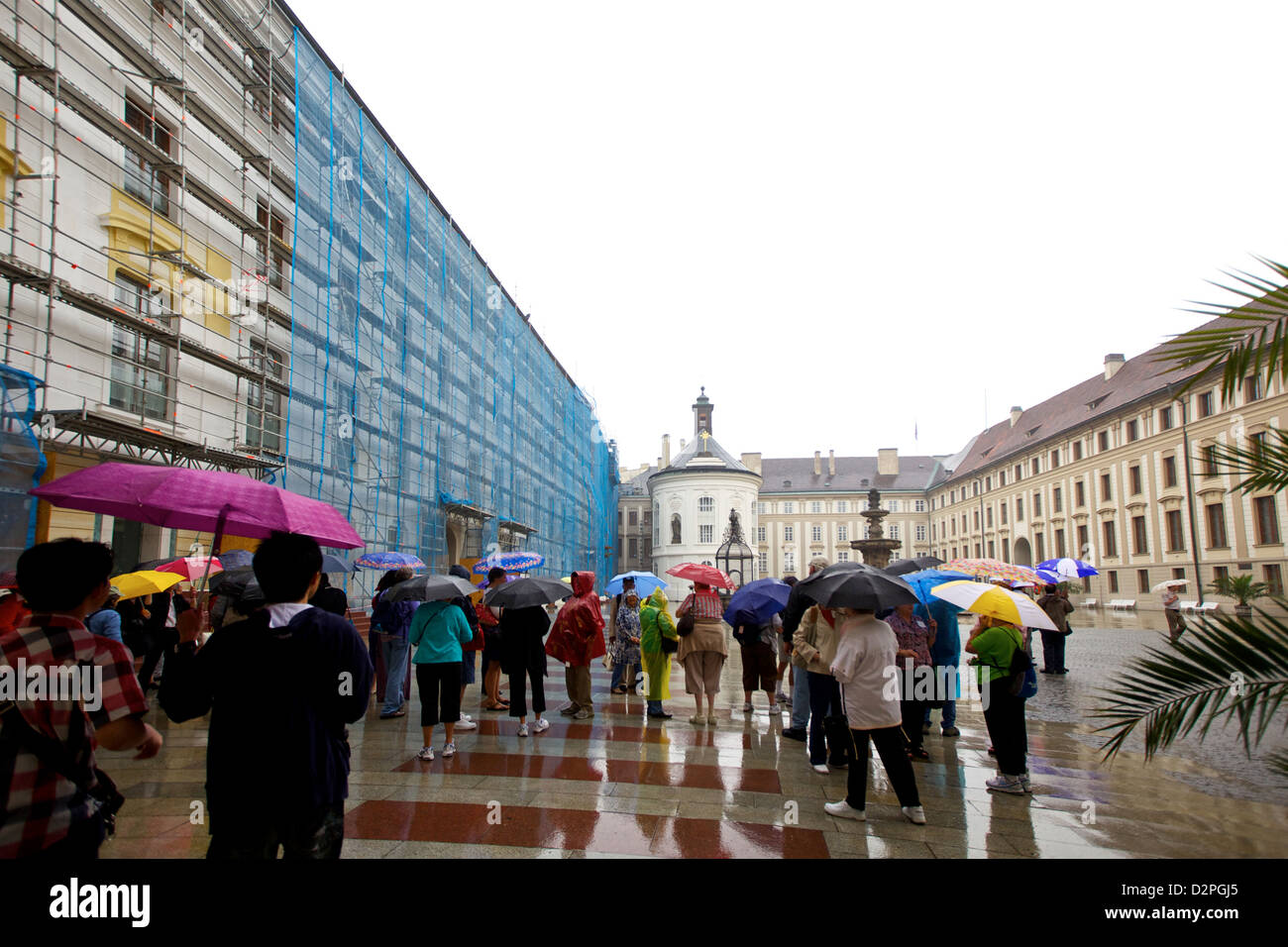 I turisti con ombrelli colorati si riuniscono in un cortile piovoso del castello di Praga, esplorando il sito storico Foto Stock