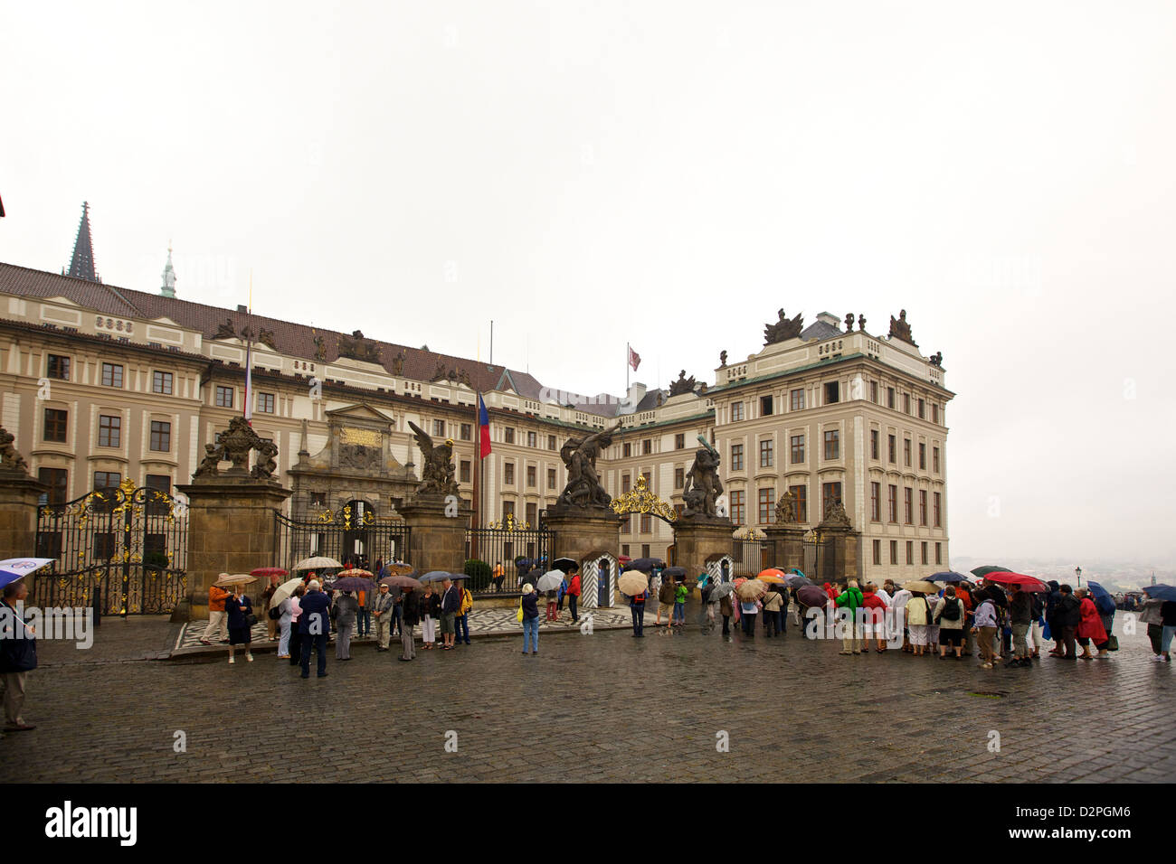 I turisti con ombrelloni si riuniscono all'ingresso del castello di Praga in una giornata di pioggia, esplorando lo storico quartiere di Hradčany nel cuore della città. Foto Stock