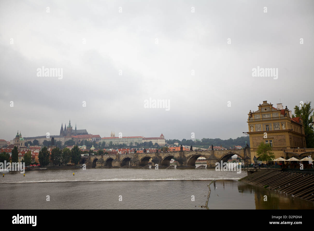 Vista panoramica del fiume Moldava con il Castello di Praga e il Ponte Carlo in lontananza sotto un cielo nuvoloso Foto Stock