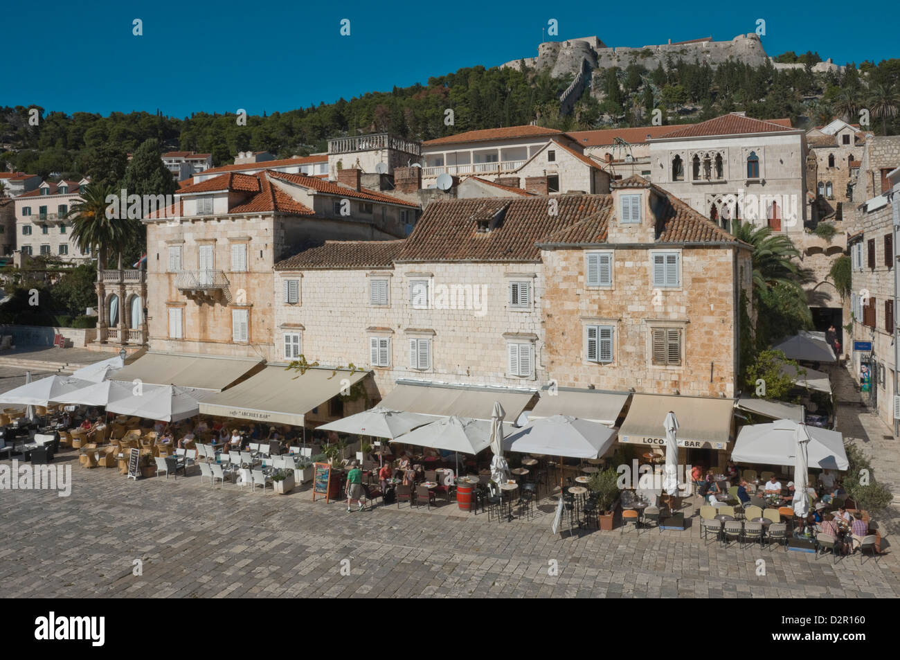 Caffè nella piazza principale, dominato dall'antica fortezza, nella città medievale di Hvar Hvar, isola della Dalmazia, Croazia Foto Stock
