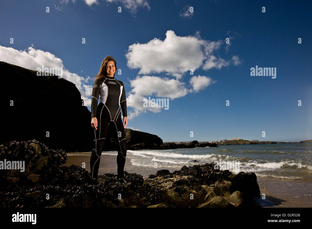Surfista femmina in piedi in wetsuit a Waters Edge, sorridente Foto Stock
