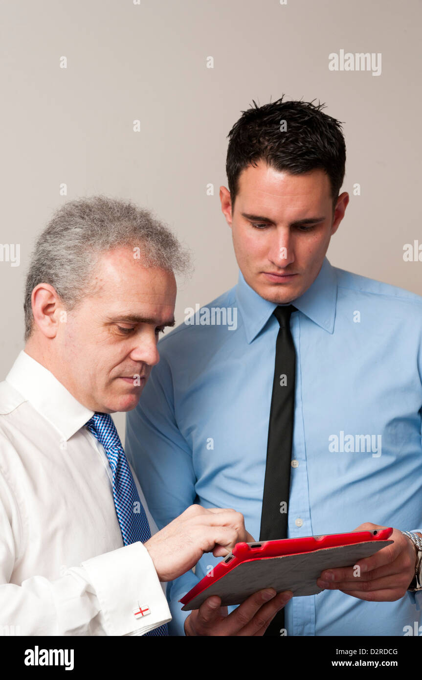 Colleghi di lavoro mentor, uno giovane e uno più vecchio, discutere il lavoro utilizzando computer tablet. Foto Stock
