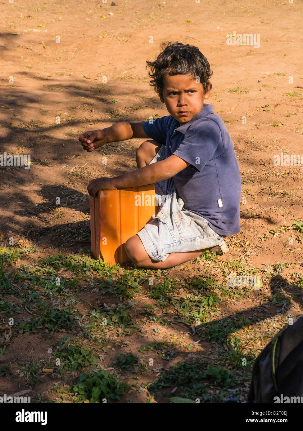 Un giovane paraguaiano ispanico boy siede sullo sporco e gioca con un blocco di ceramica utilizzati nella costruzione della casa. Foto Stock