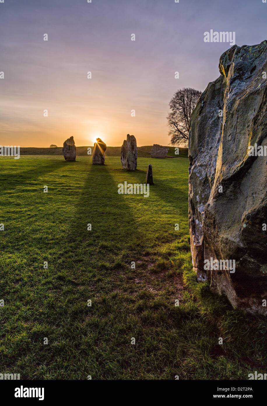 Il sole sorge alle spalle di una parte del grande cerchio di pietre di Avebury, Wiltshire, Regno Unito casting lunghe ombre attraverso il terreno. Foto Stock