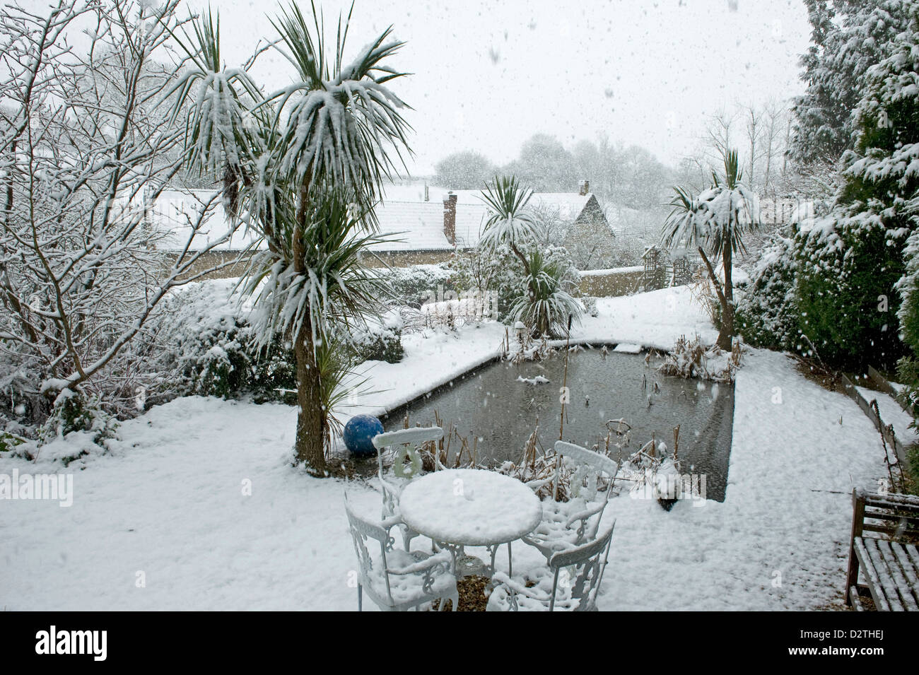 Laghetto in giardino, tavolo, sedie e arbusti in una forte tempesta di neve, Devon, Foto Stock