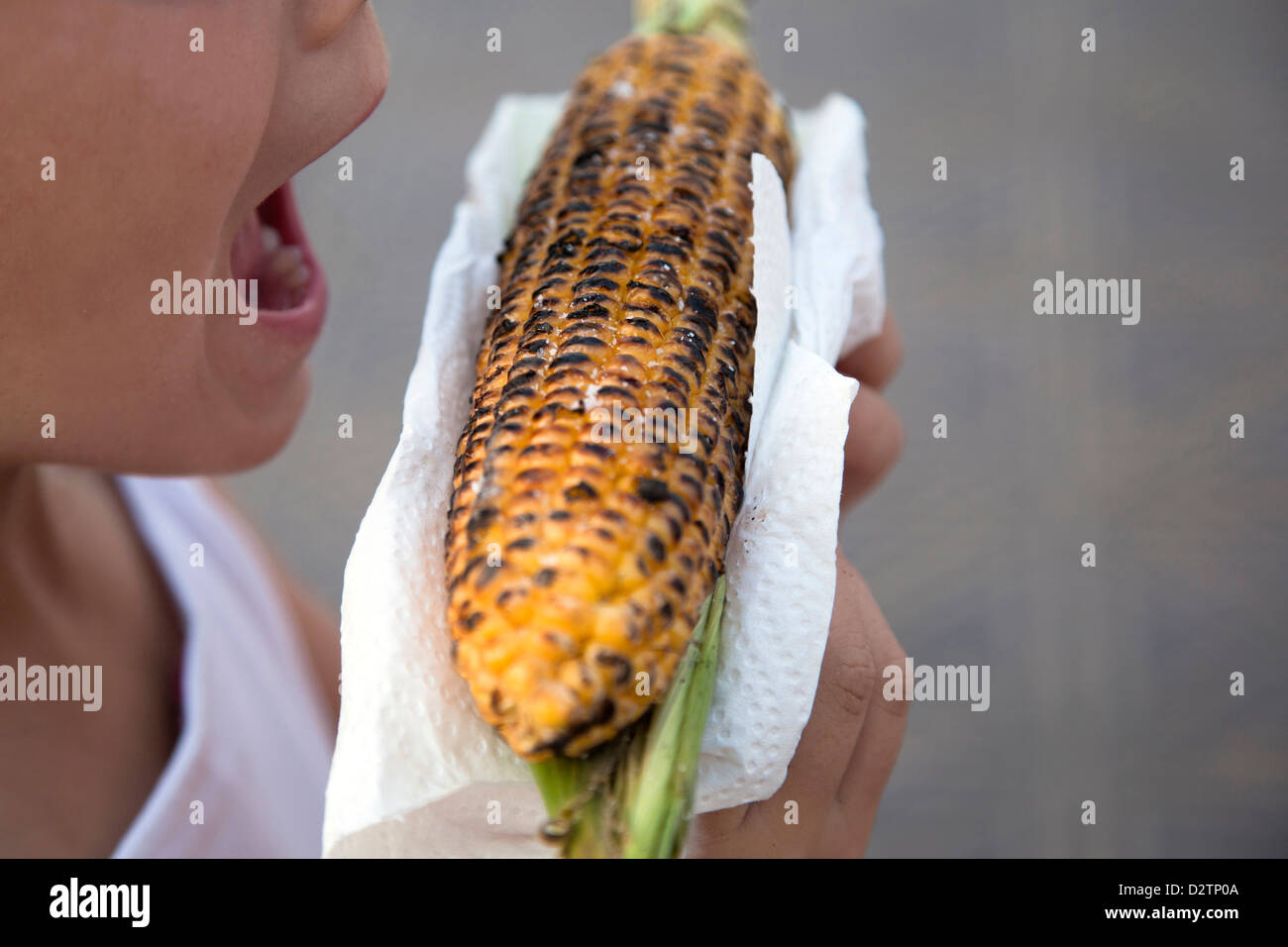 Girl circa a mordere un orecchio di grigliate di mais. Foto Stock