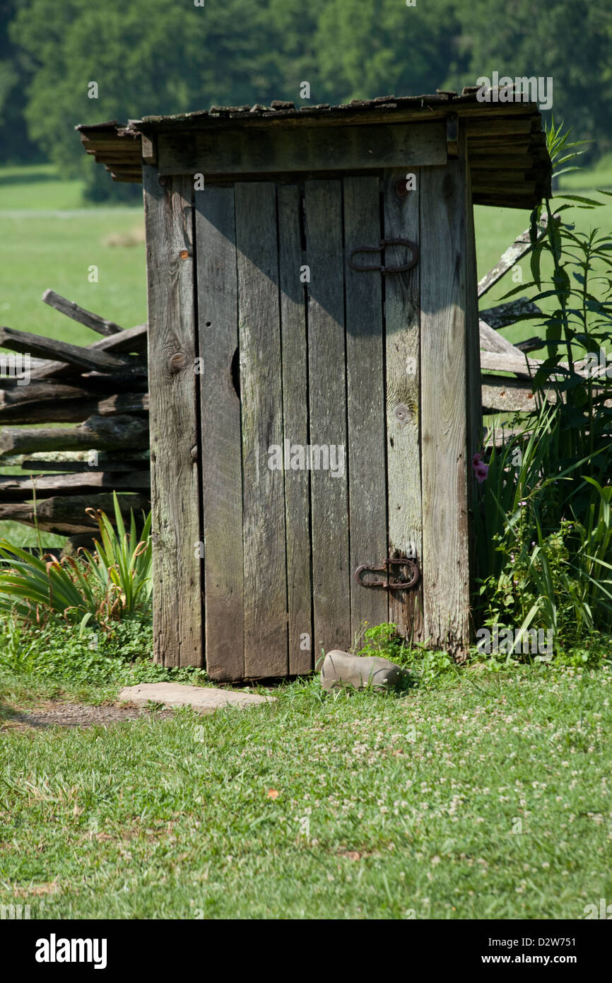 In legno antico dipendenza, fatta di grezzo di pannelli di legno e Ferri da cavallo per cerniere, in un campo verde di boschi in background Foto Stock