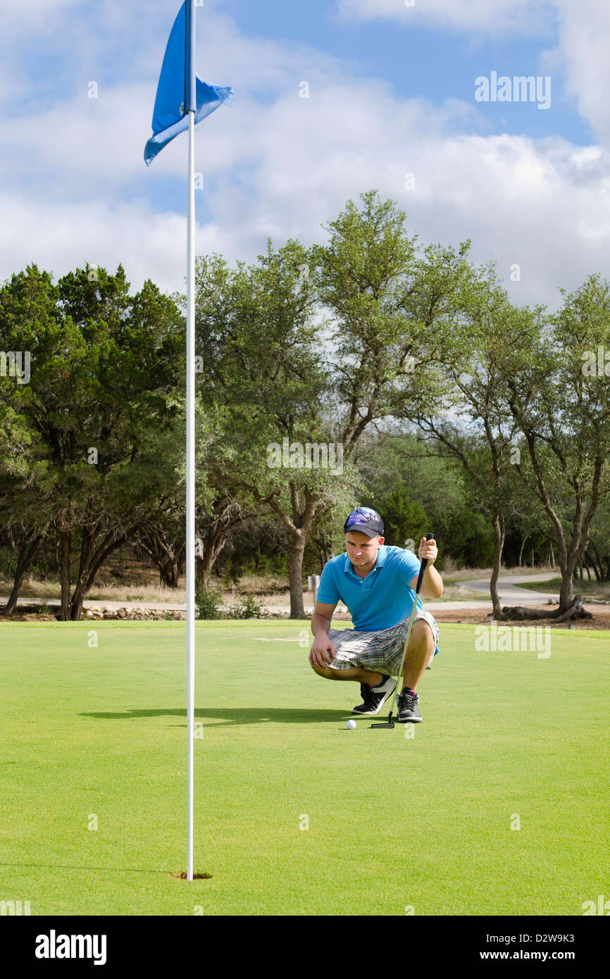 Giovane uomo accovacciata alla figura fuori il meglio possibile colpo a un campo da golf Foto Stock