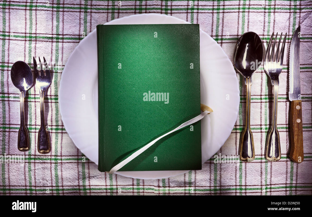 Vecchio libro verde sulla piastra bianca, accessori su entrambi i lati. Immagine concettuale di un libro come cibo. Foto Stock