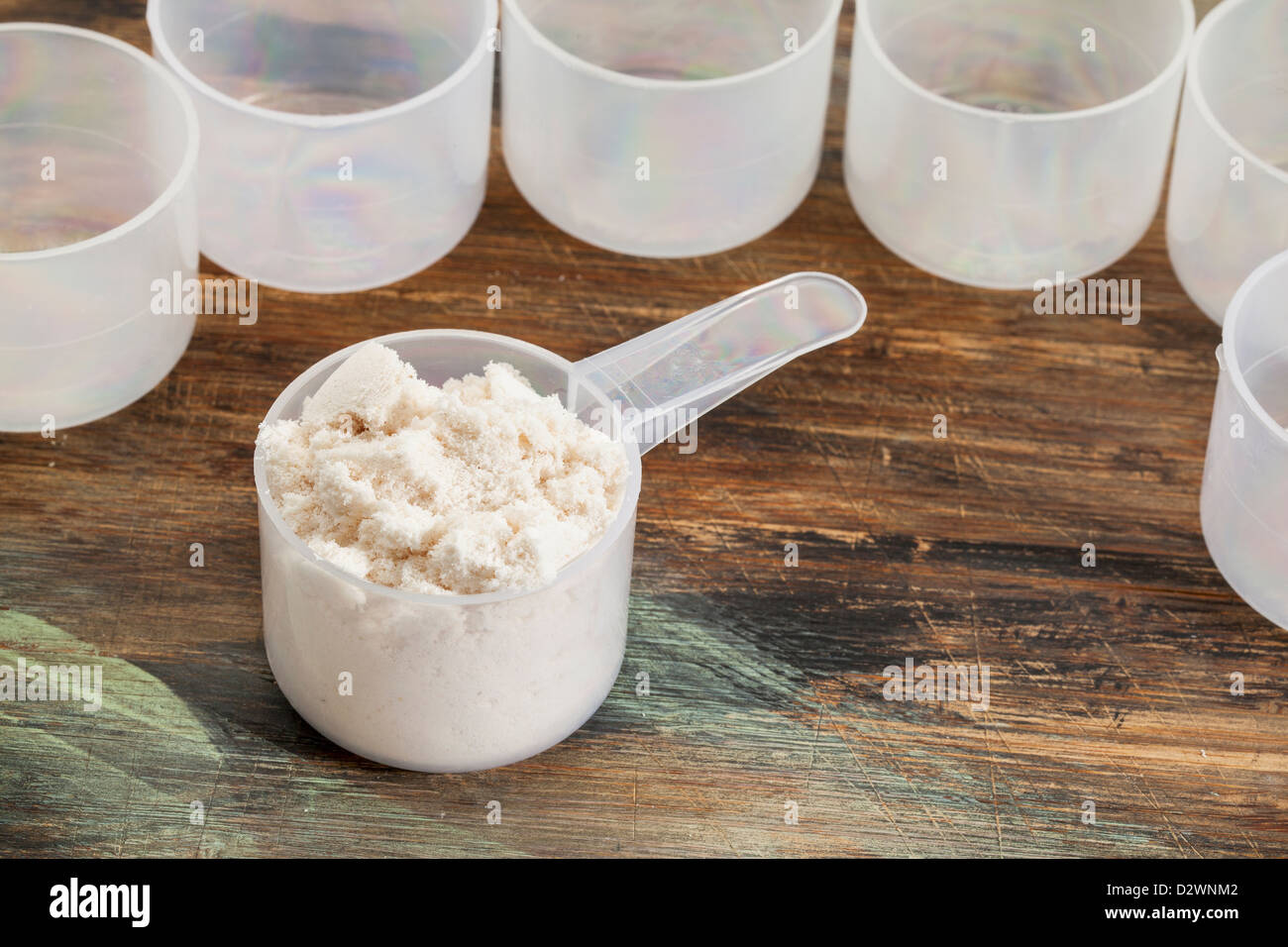 Scoop di proteina di siero di latte in polvere su di una superficie di legno circondato da vuoto i convogliatori in plastica Foto Stock