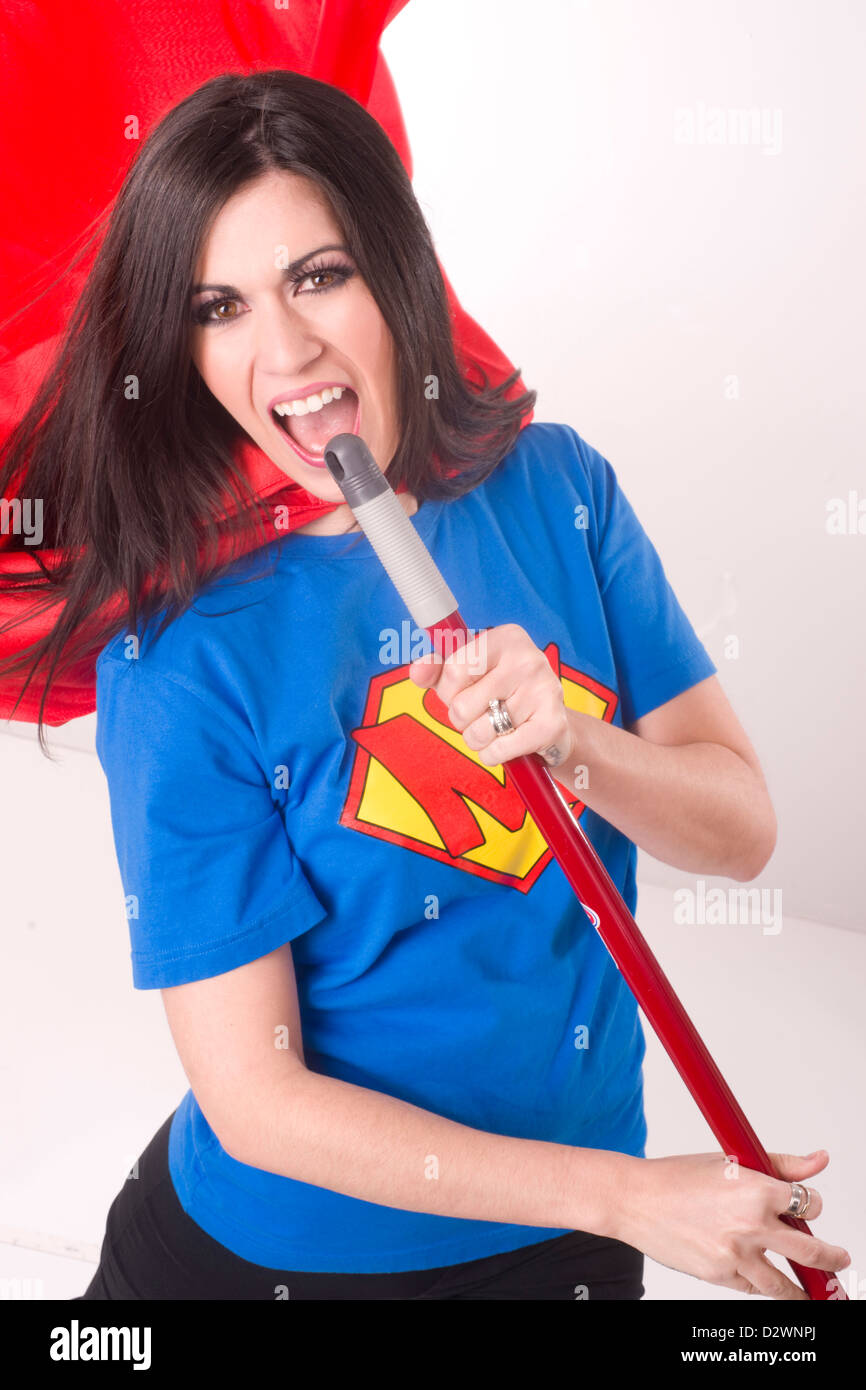 Una bella donna di crested shirt e red cape lipsyncs con il suo bastone di scopa durante la pulizia Foto Stock