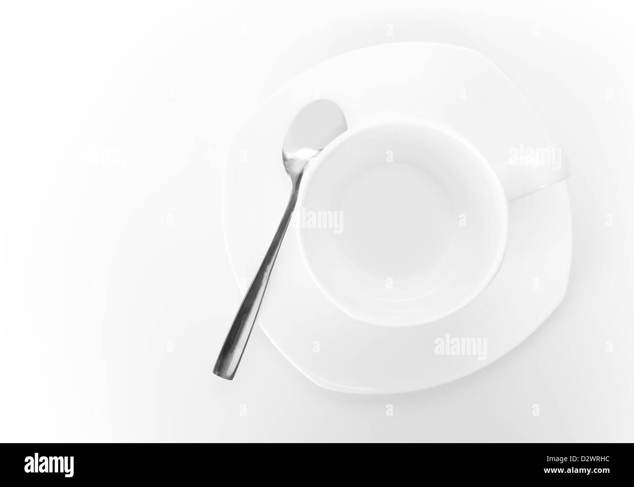 White tazza di ceramica sul piattino con cucchiaio di metallo al di sopra di uno sfondo bianco. Vista superiore Foto Stock