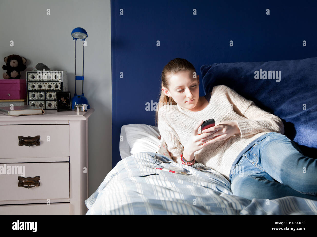 Giovane ragazza adolescente per la messaggistica di testo dal suo letto in camera da letto Foto Stock