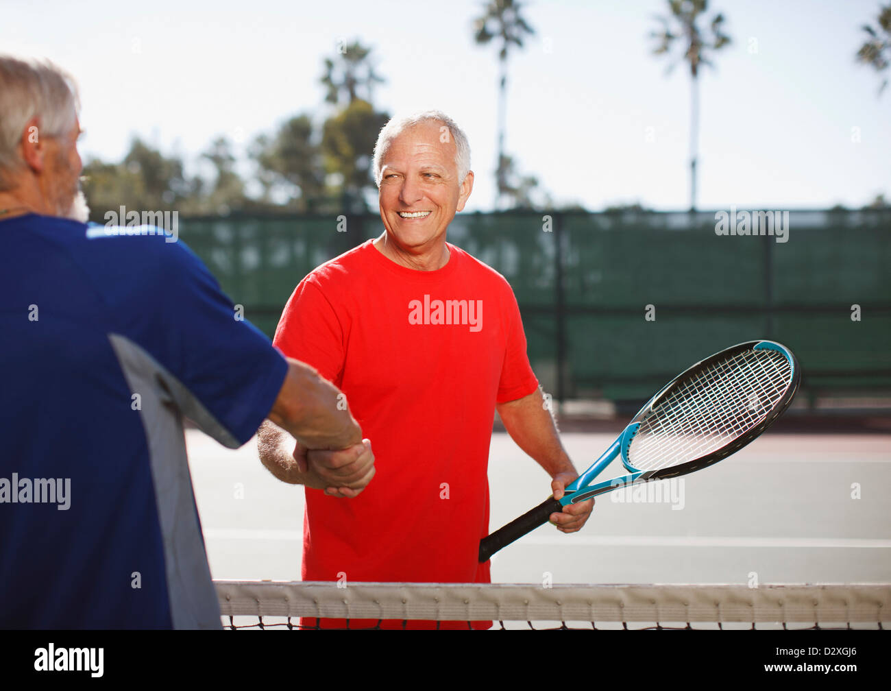 Gli uomini più anziani si stringono la mano sul campo da tennis Foto Stock
