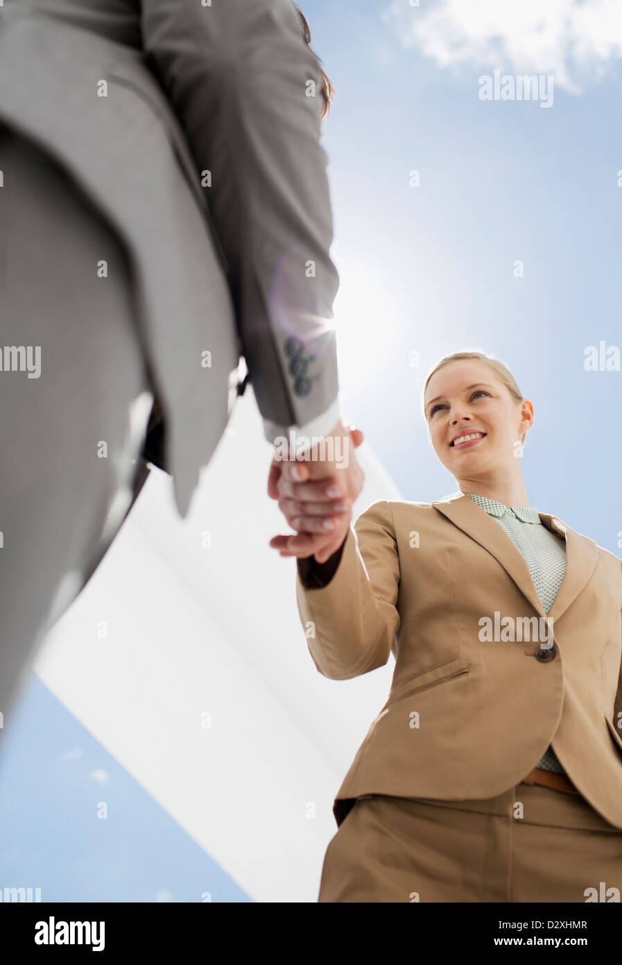 Imprenditore e imprenditrice stringono le mani sotto il cielo blu Foto Stock