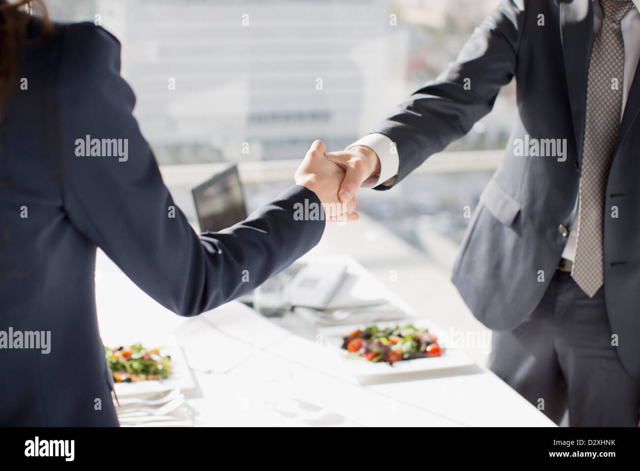 Imprenditore e imprenditrice stringono le mani a tavola con pranzo Foto Stock