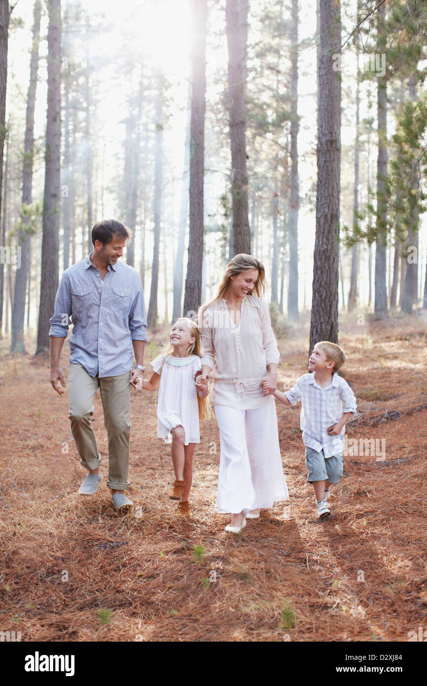 La famiglia felice tenendo le mani e camminare nei boschi di sole Foto Stock