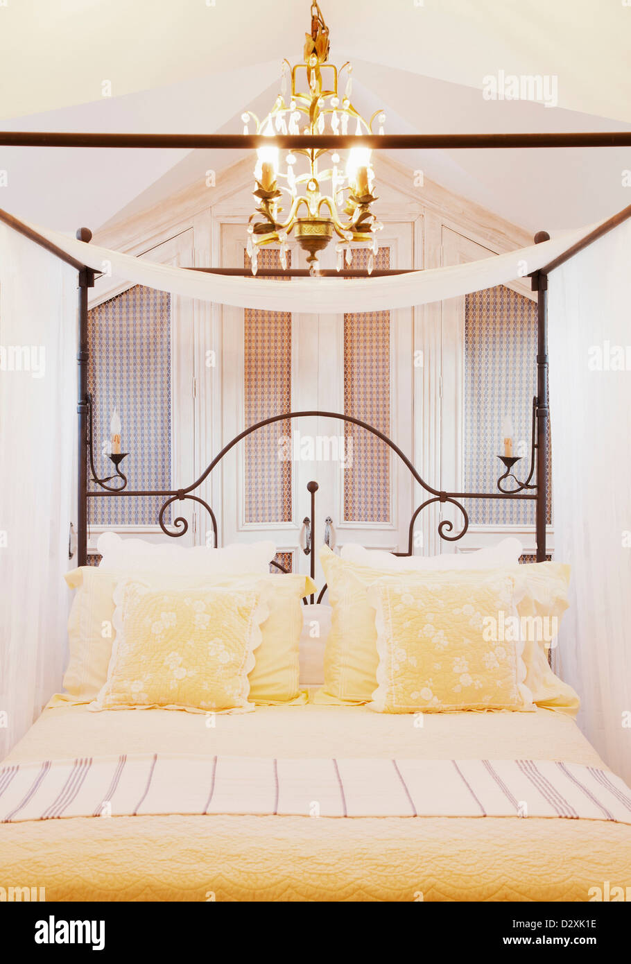 Lampadario sopra il letto a baldacchino con biancheria di colore giallo Foto Stock