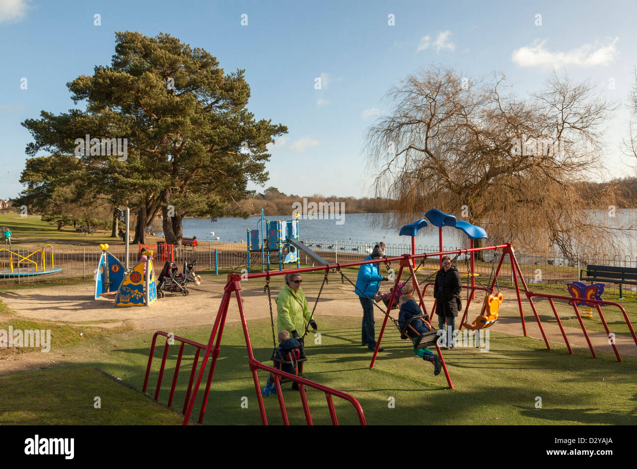 I genitori e i bambini utilizzando oscilla in area gioco per bambini a Petersfield Lago Foto Stock