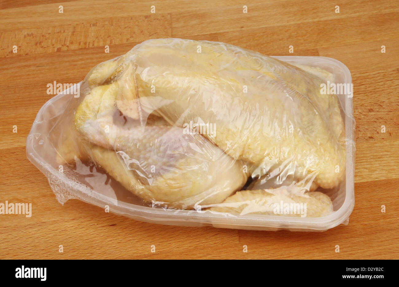 Tutto il pollo crudo imballaggi in plastica su una cucina in legno piano di lavoro Foto Stock