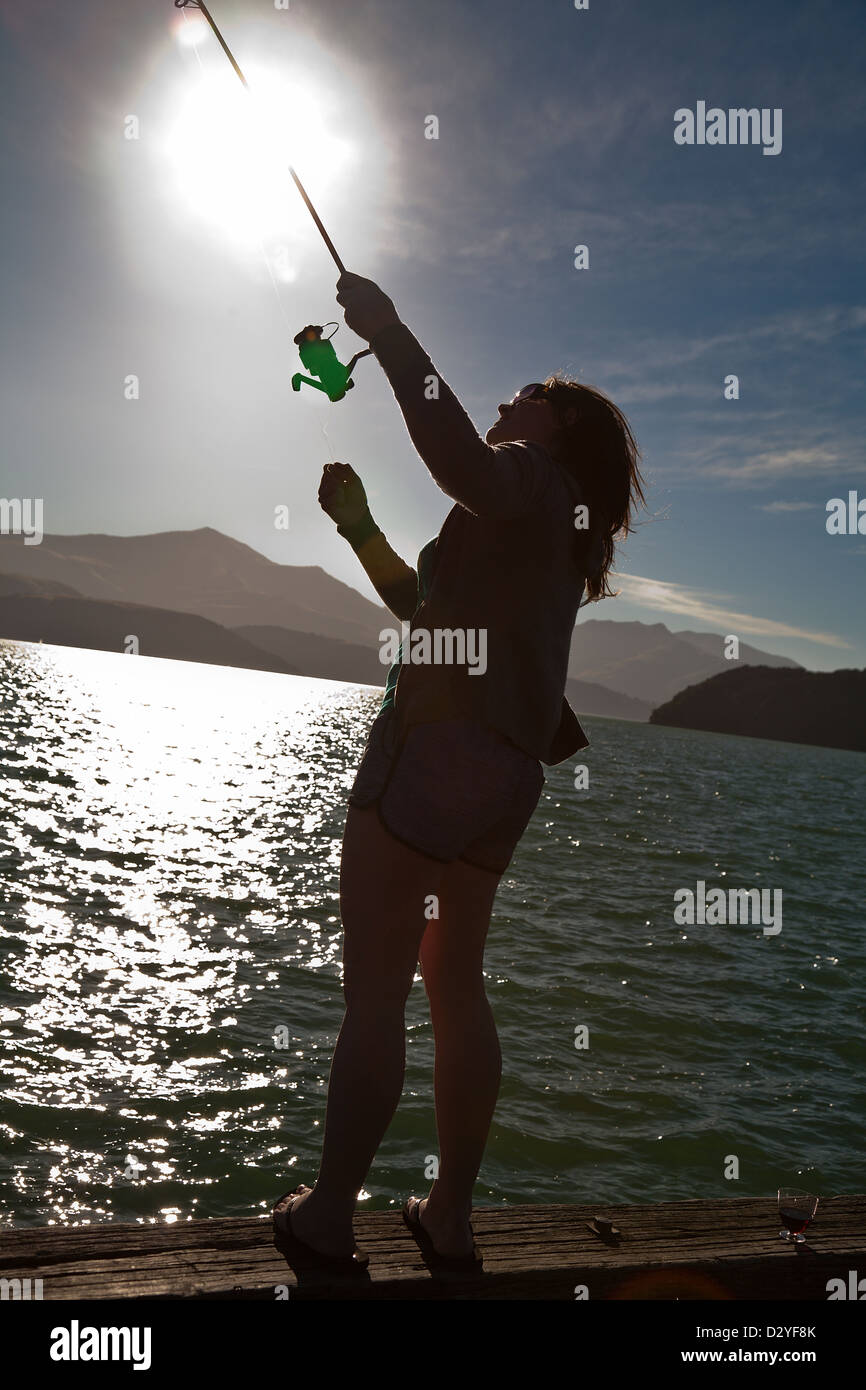 Una giovane donna di pesca al largo di un pontone a Akaroa, Canterbury, Isola del Sud, Nuova Zelanda Foto Stock