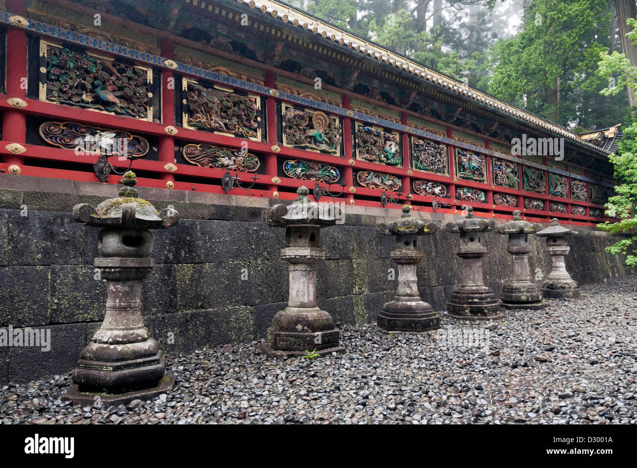 Fila di antiche lanterne di pietra vicino al rosso scenic parete del tempio giapponese Foto Stock