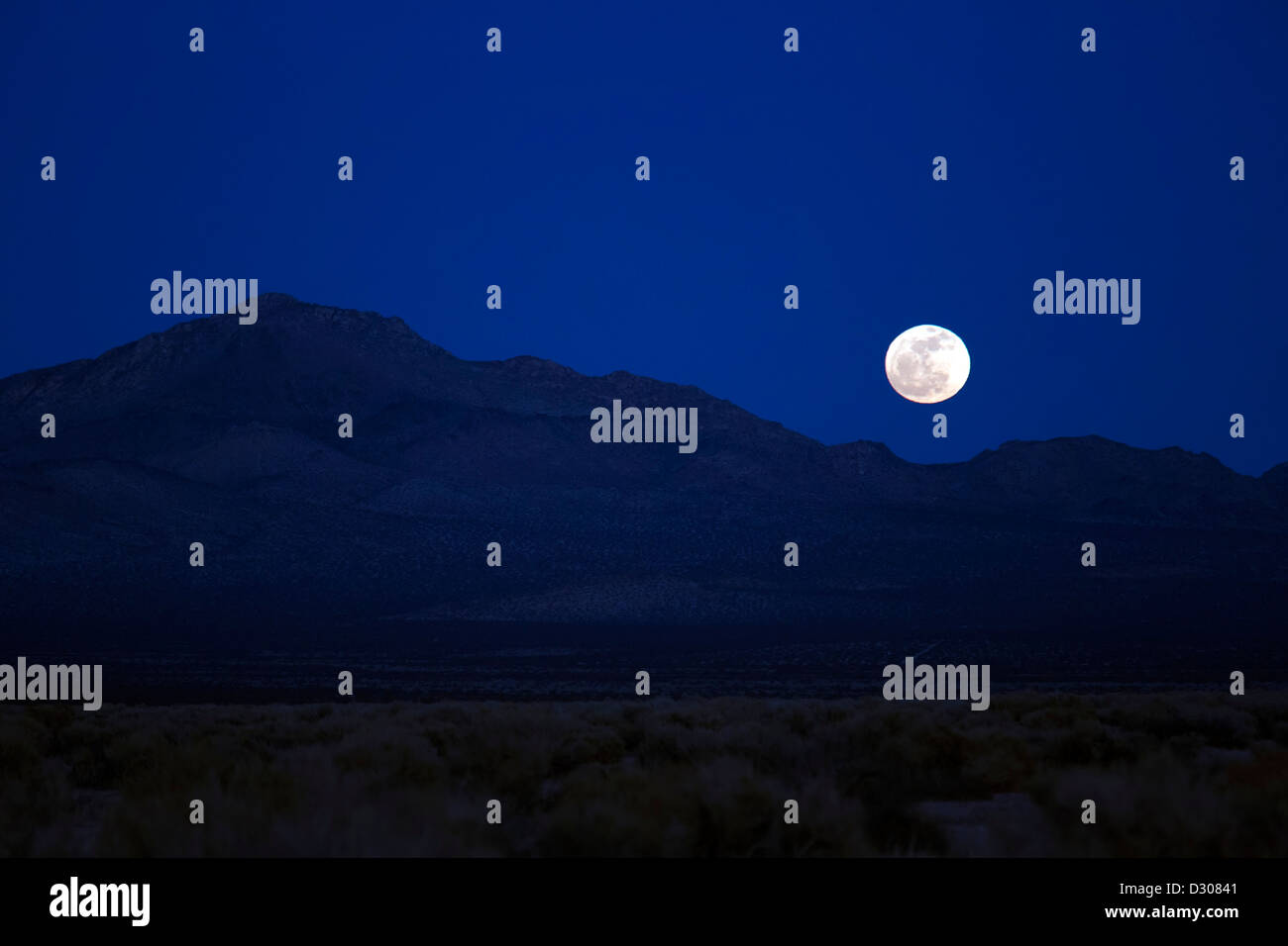 Kramer Junction, California - la luna piena sorge su Fremont picco nel deserto di Mojave. Foto Stock