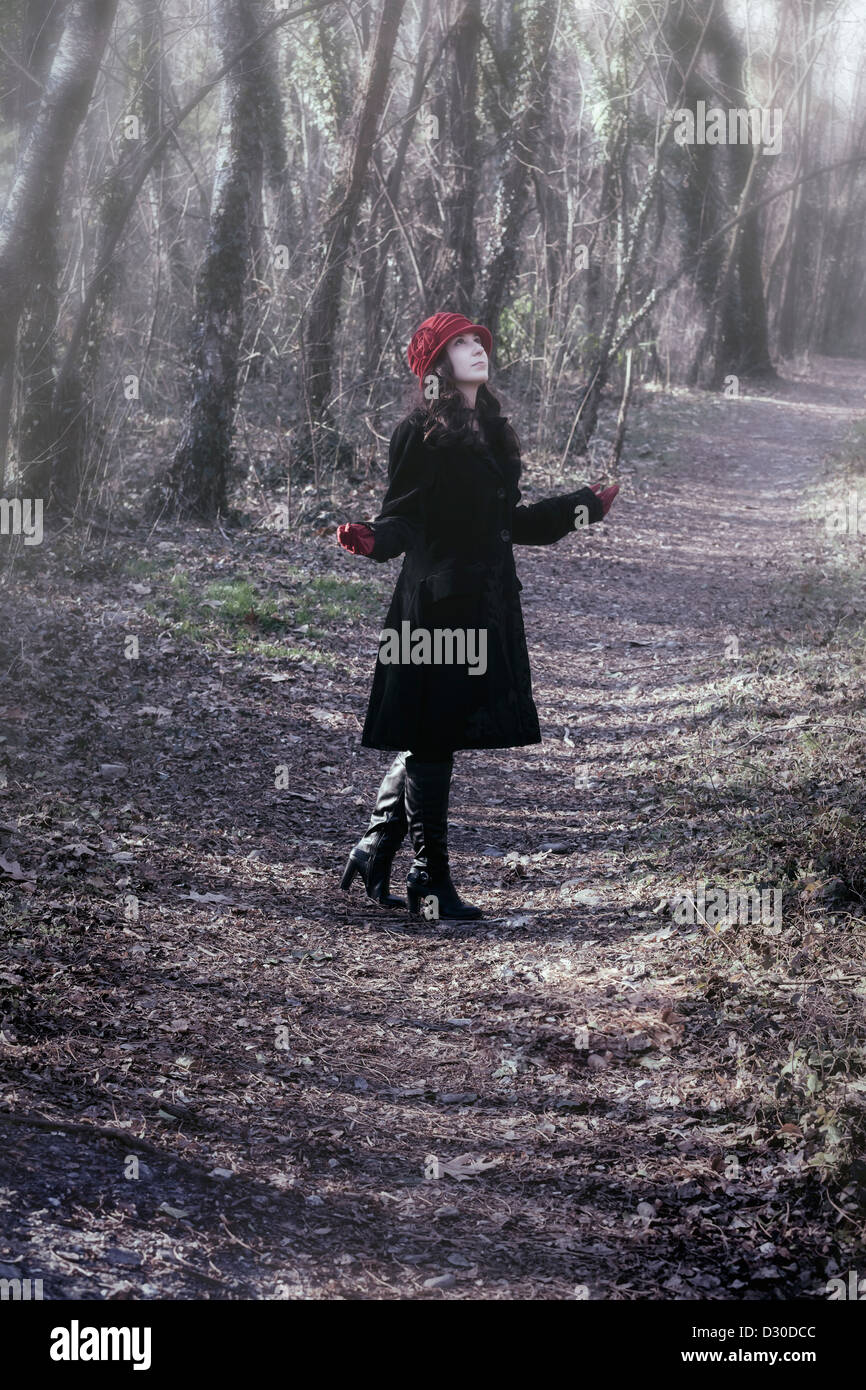 Una donna in un mantello nero con Red Hat è in piedi nel bosco Foto Stock