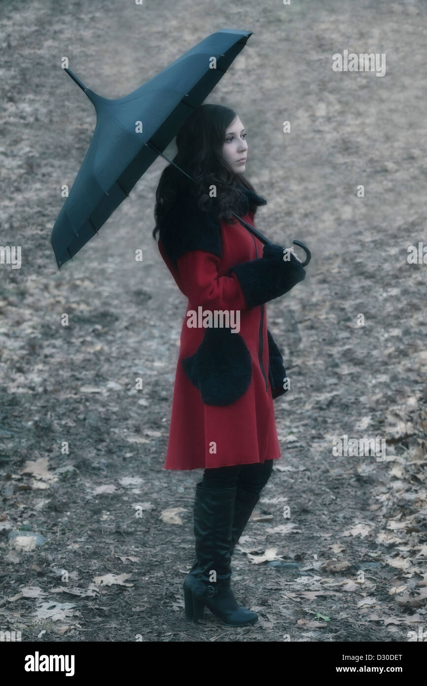 Una donna con un cappotto rosso e un ombrello è camminare su una pista forestale Foto Stock