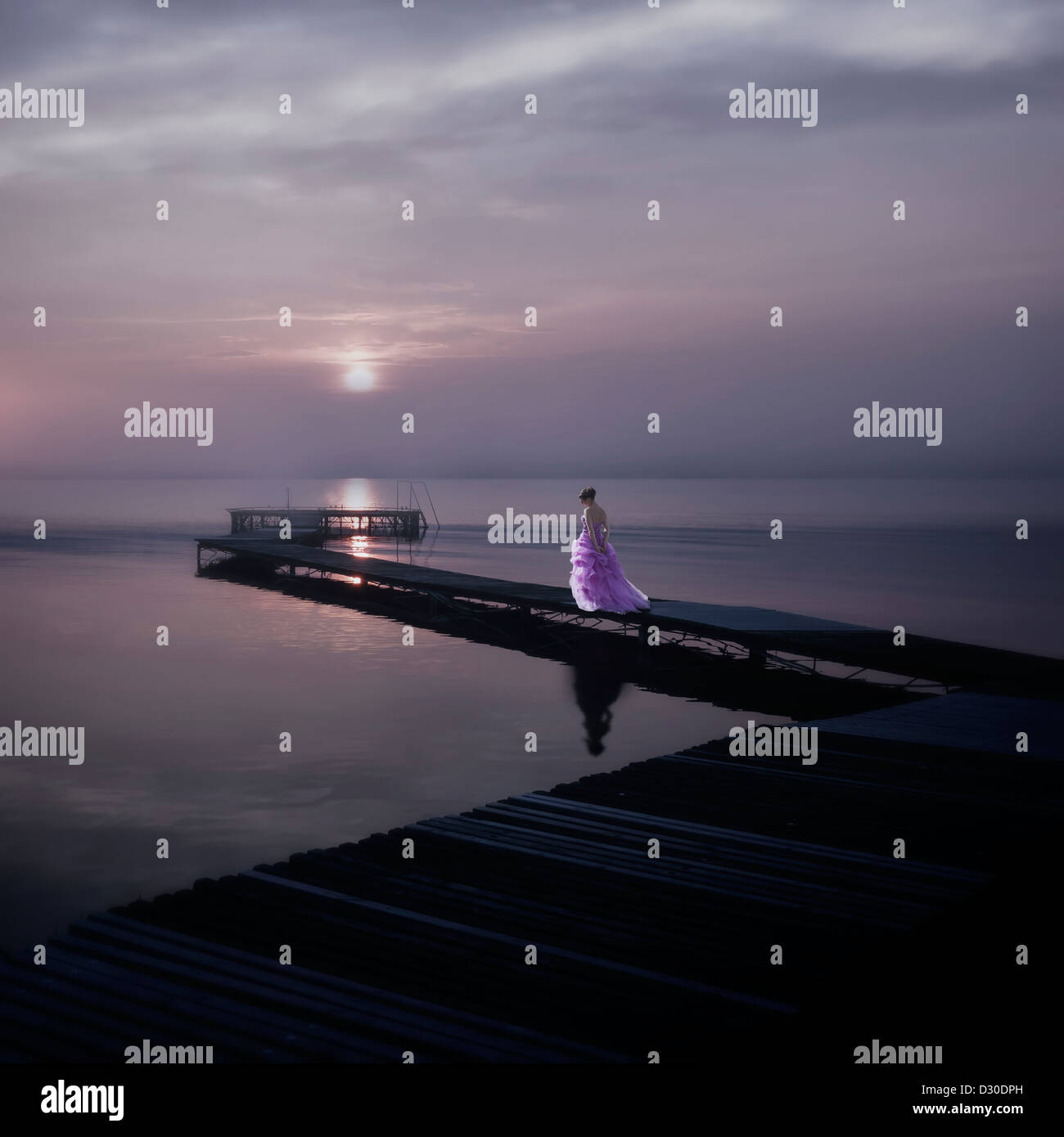 Una donna in un elegante abito rosa su una passerella su un lago durante il tramonto Foto Stock