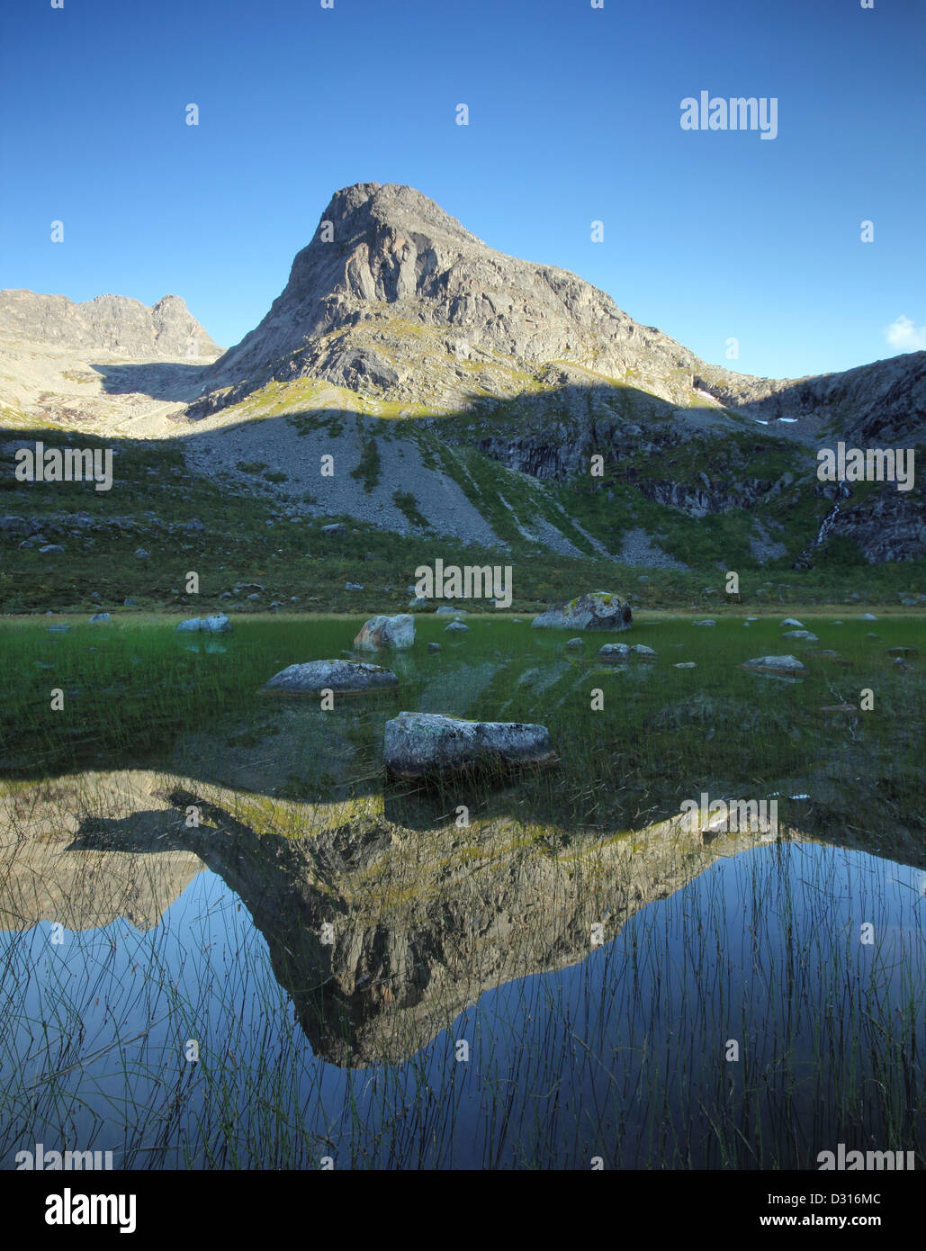 Sole alto picco di montagna riflessa in un lago glaciale al di sopra del Circolo Polare Artico in Norvegia del nord. Foto Stock