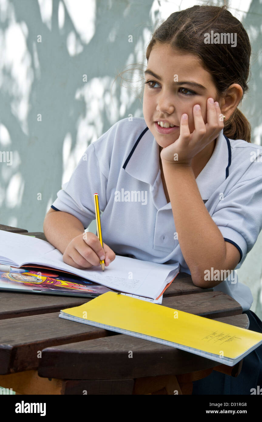 Junior ispanico schoolgirl pause a daydream durante il suo esame della scuola al di fuori di studi nella scuola di sole parco giochi Foto Stock