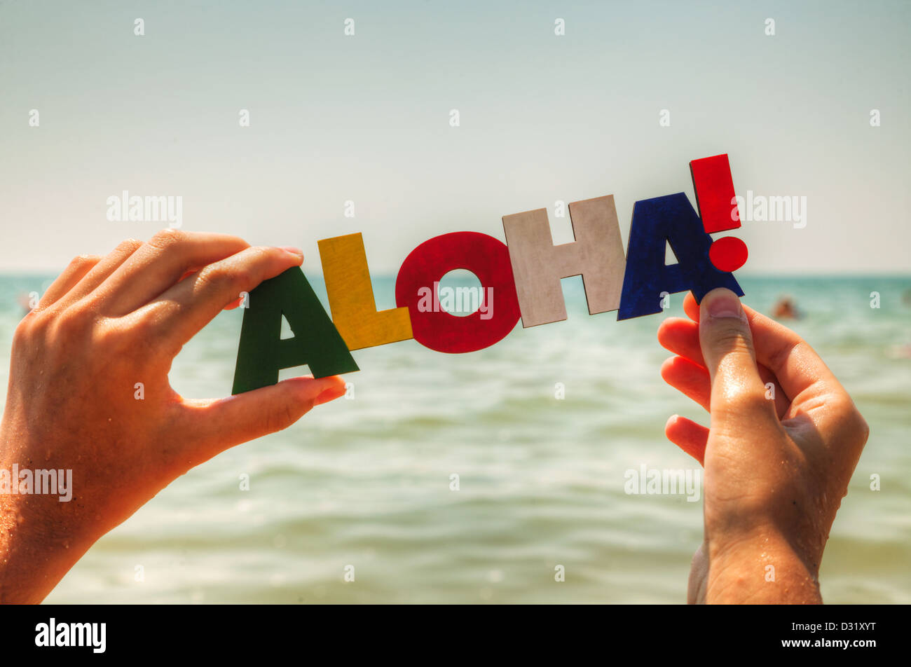 La femmina mano azienda colorita parola "Aloha" contro sfondo blu Foto Stock