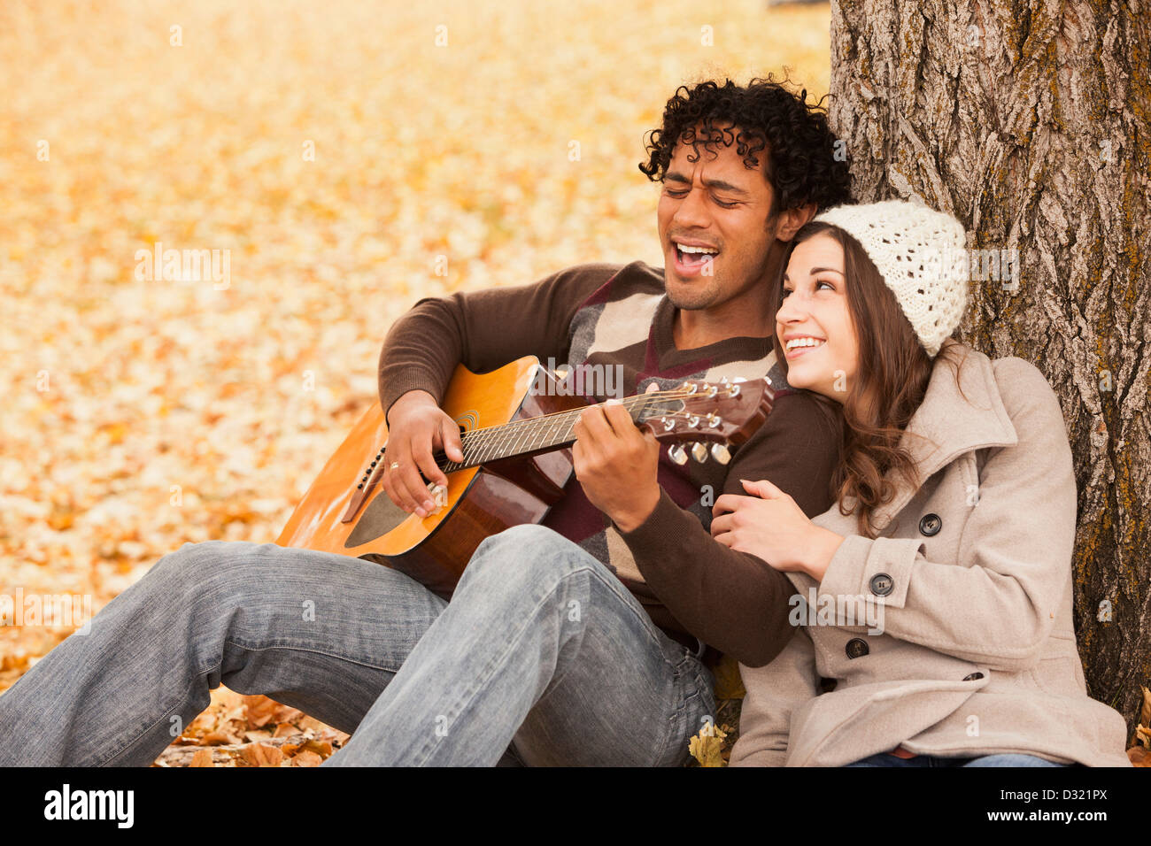 Uomo a suonare la chitarra per ragazza in foglie di autunno Foto Stock