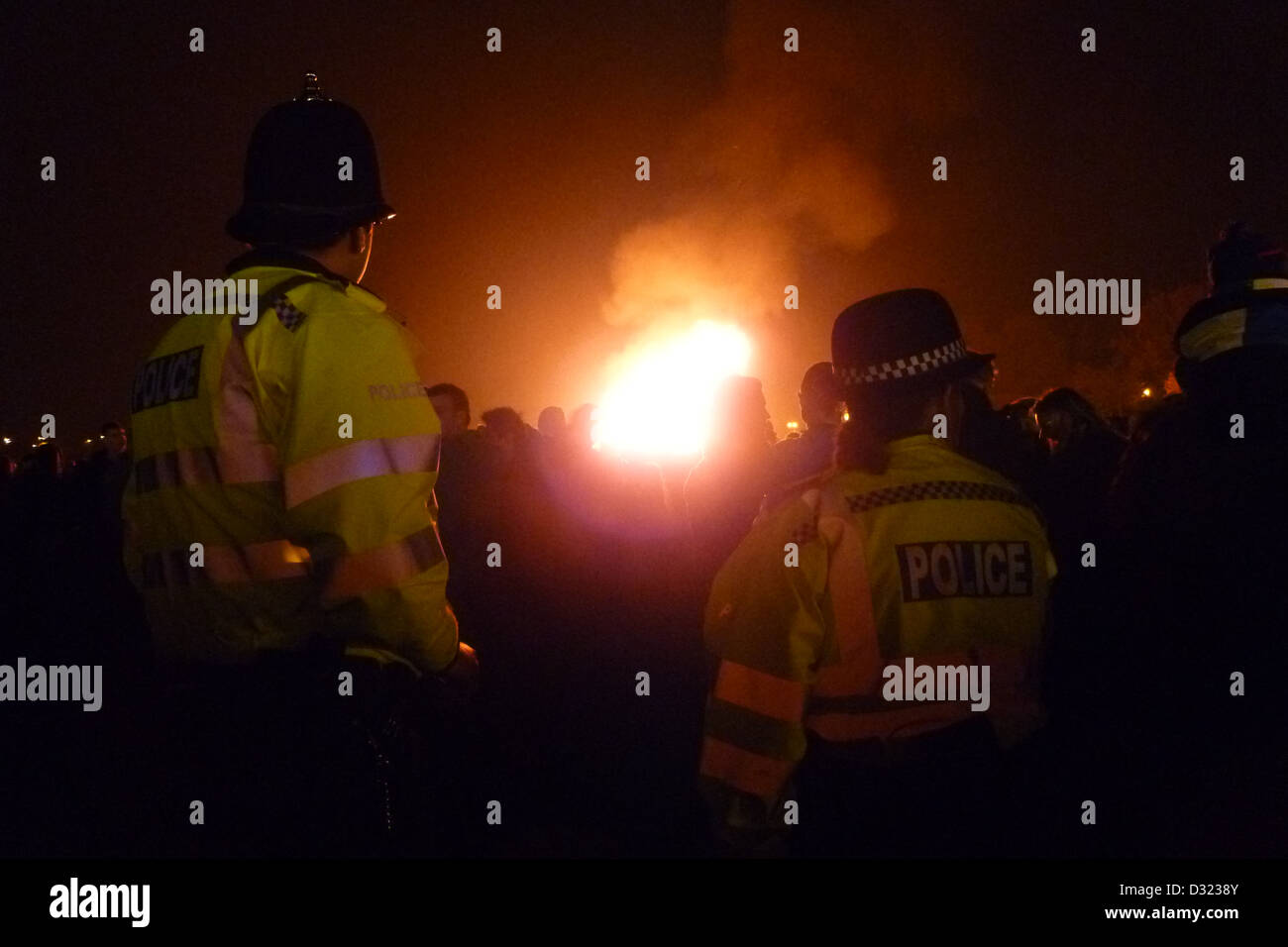 Un maschio e femmina poliziotto e poliziotta guardando un grande incendio o danni di tumulto con grandi folle che indossa giacche catarifrangenti. Foto Stock