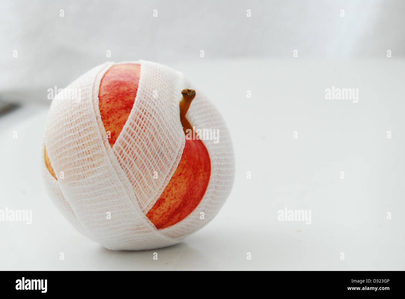 Un rosso e giallo Apple su uno sfondo bianco, avvolto in una garza bianca benda con un sopra o birds eye view del frutto. Foto Stock