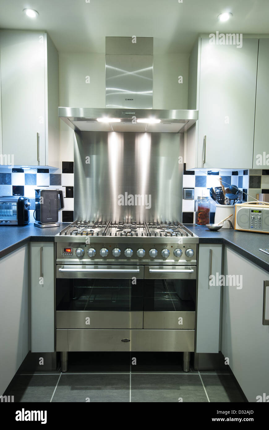 Un moderno gas + gamma elettrica fornello con estrattore e splashback in una piccola cucina contemporanea. Regno Unito, 2013. Foto Stock