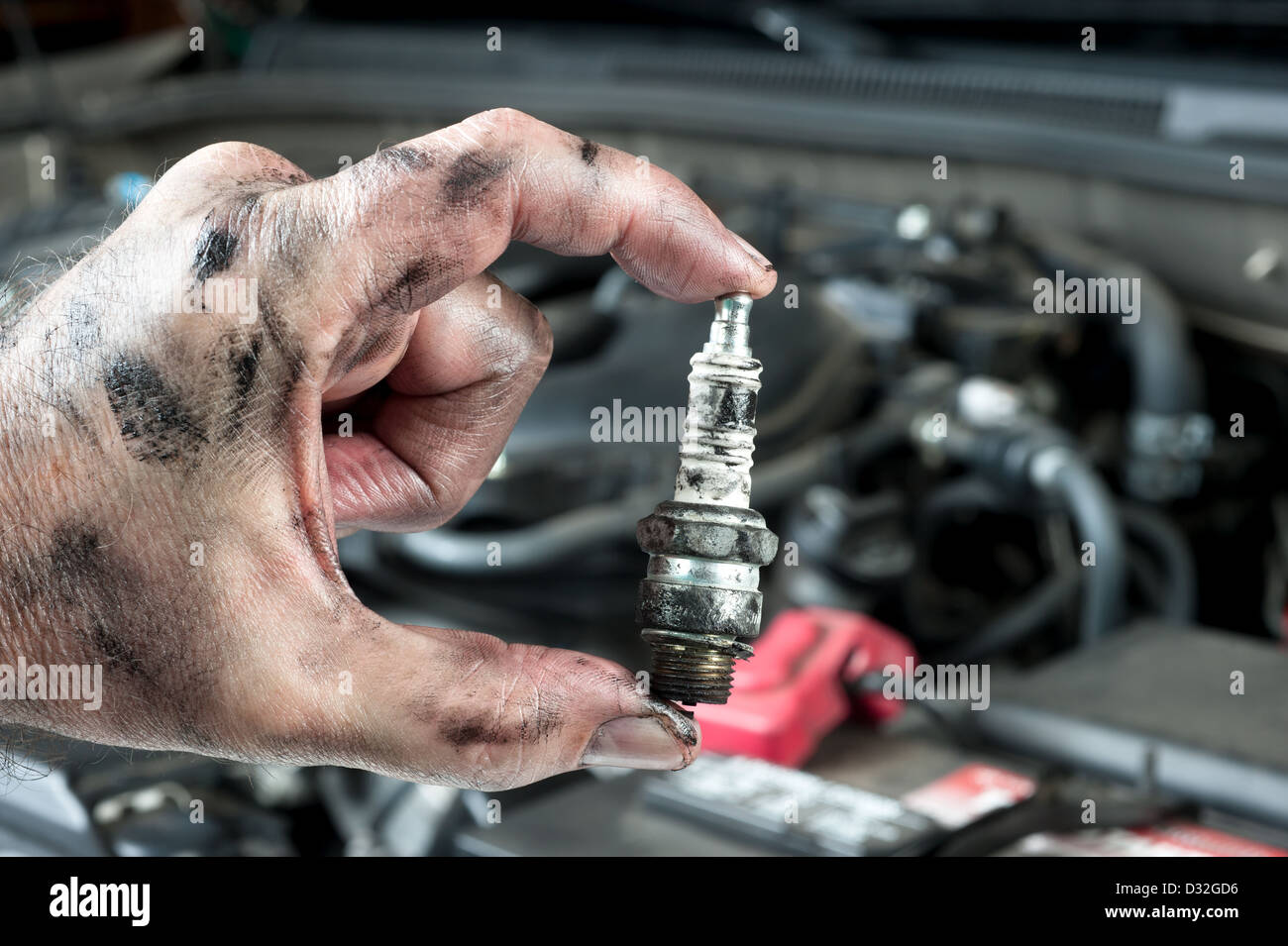 Un meccanico automatico mantiene un vecchio e sporco candela oltre il motore di una macchina è tuning up. Foto Stock