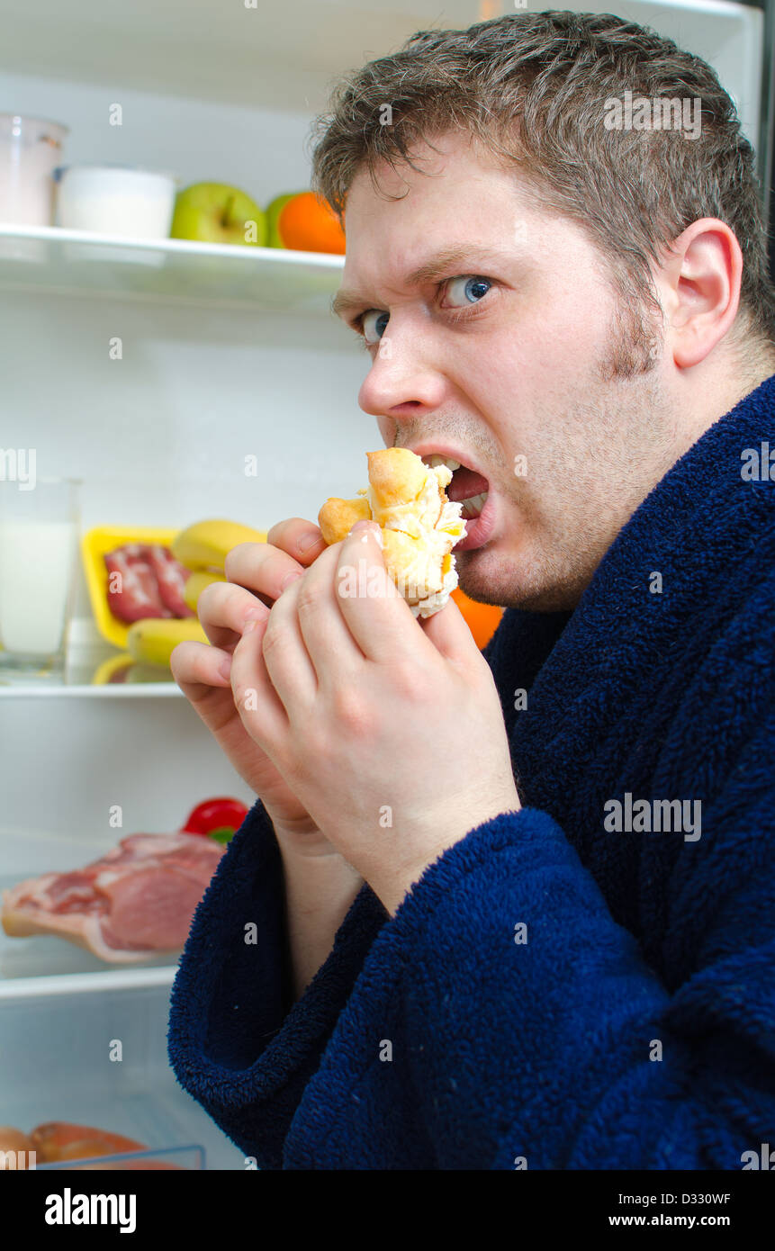 Uomo bello mangiare una fetta di torta vicino al frigorifero aperto Foto Stock